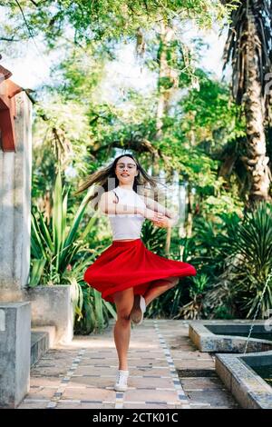 Young woman dancing on footpath against trees in park Stock Photo