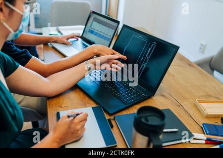 Programmers discussing over laptop while wearing protective face mask at office during coronavirus Stock Photo