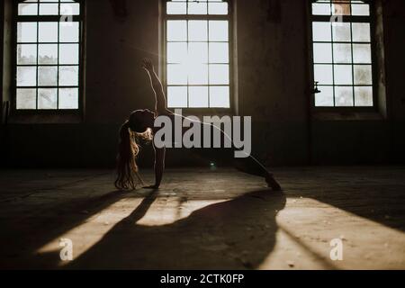 Silhouette of woman doing side plank on floor at abandoned factory Stock Photo