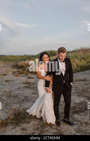 Smiling bridegroom holding hands while walking in field Stock Photo