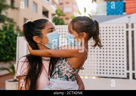 Mother holding daughter wearing mask while standing outdoors Stock Photo