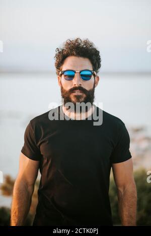 Bearded man wearing sunglasses while standing against lake Stock Photo