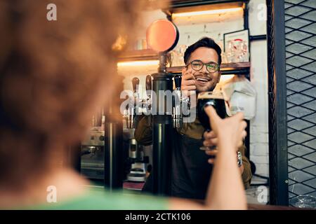 Barkeeper handing over glass of beer to woman in a pub Stock Photo