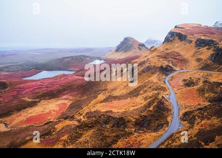 UK, Scotland, Drone view of empty highway stretching along brown mountainous landscape of Isle of Skye with small lakes in background Stock Photo