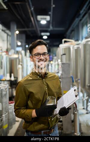 Portrait of happy man holding clipboard and beer glass in craft brewery Stock Photo