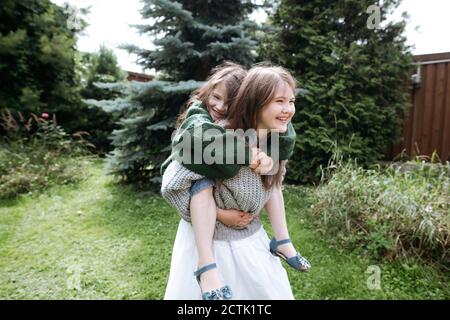 Girl giving piggyback ride sister in back yard Stock Photo