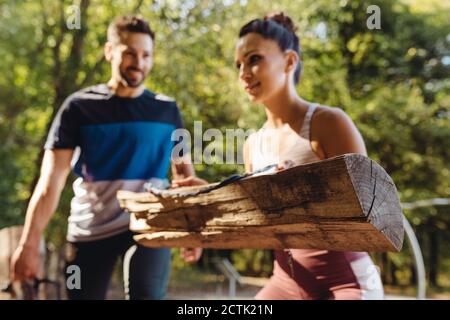 Woman and man lifting up heavy logs on a fitness trail