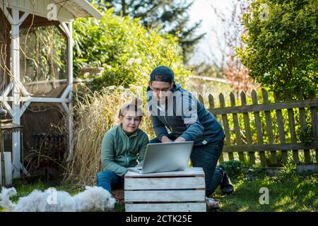 Father teaching daughter while using laptop in yard Stock Photo