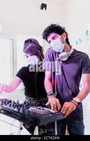 DJing couple wearing face masks while mixing sound at recording studio Stock Photo