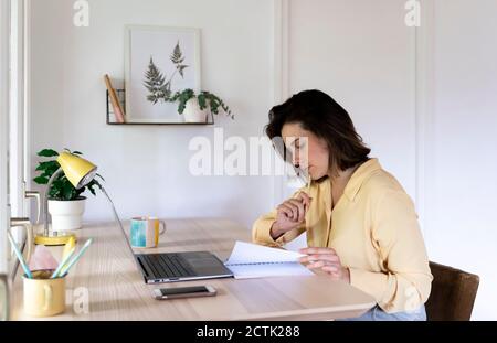 Young female entrepreneur looking at diary while sitting with laptop Stock Photo