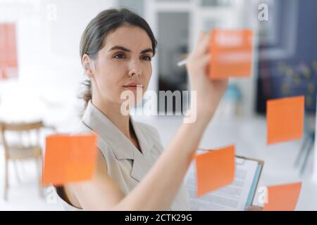 Woman writing on sticky note while standing at office Stock Photo