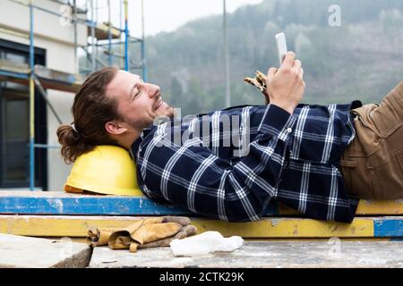 Construction worker using smart phone while eating food on wood at construction site Stock Photo