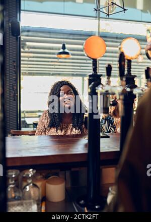 Smiling young woman sitting at the counter in a pub Stock Photo