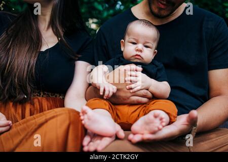 Cute baby boy sitting on father's lap by mother at park Stock Photo