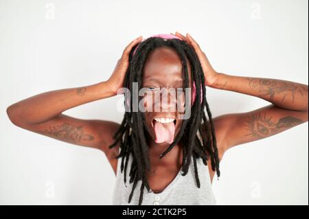 Woman with headphone showing her forked tongue against white background Stock Photo