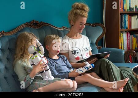 Woman using digital tablet while kids with robots sitting on sofa in living room at home Stock Photo