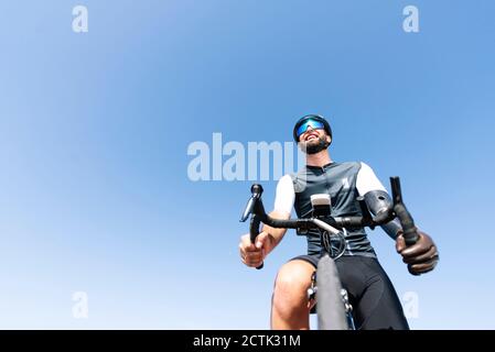 Male amputee cyclist with artificial limb riding bicycle against clear sky Stock Photo