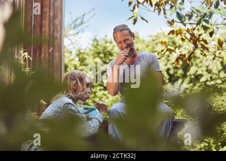 Smiling father looking at daughter while brushing teeth with her in yard Stock Photo