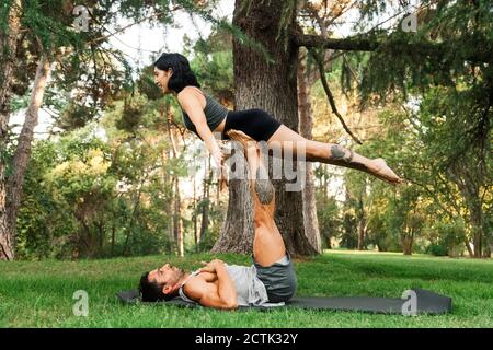 Man balancing girlfriend on legs while practicing acroyoga in park Stock Photo