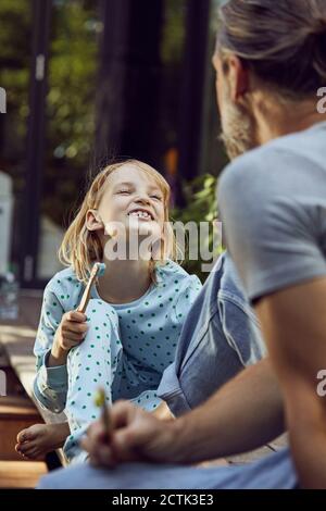 Girl showing teeth to father while brushing with him in yard Stock Photo