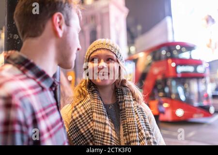 Young couple talking while standing at Piccadilly Circus with double-decker bus in background Stock Photo