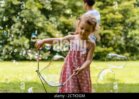 Cute baby girl making bubble with brother in background at park Stock Photo