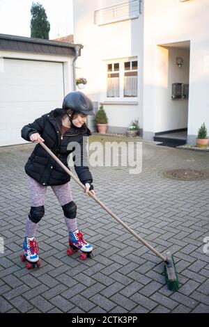 Girl skating while cleaning porch with broom Stock Photo