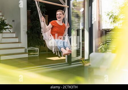 Cheerful woman with short hair laughing while swinging against house in porch Stock Photo