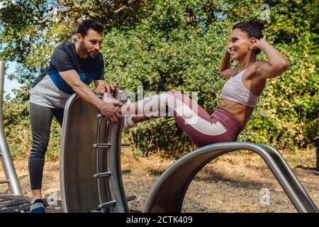 Man supporting woman doing exercises on a fitness trail Stock Photo