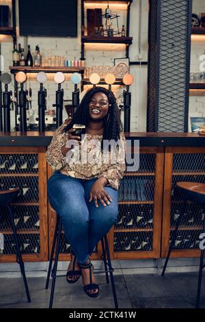 Happy woman sitting at the counter in a pub having a beer Stock Photo