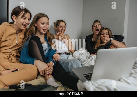 Group of girlfriends sitting on bed, watching movie on laptop Stock Photo