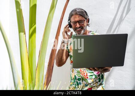 Smiling man using laptop while standing by Stock Photo