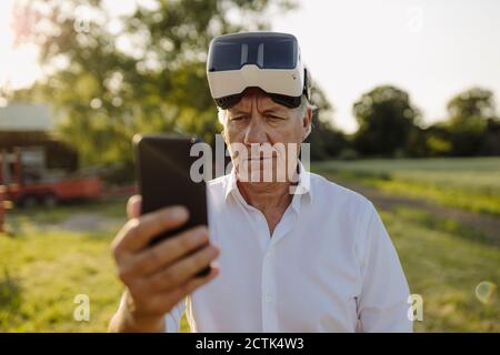 Man using smart phone while wearing VR glasses in yard Stock Photo