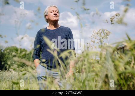 Wrinkled man with eyes closed holding laptop in agricultural field Stock Photo