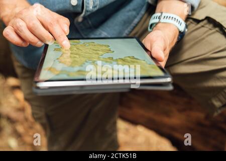 Close-up of man's hands using map over digital tablet in forest Stock Photo