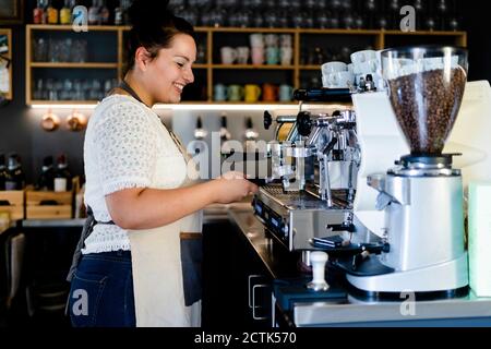 Smiling female barista making coffee through machine in cafe Stock Photo