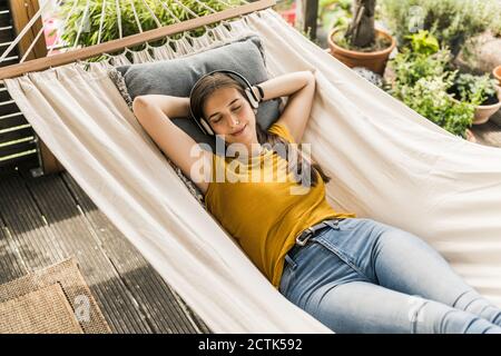 Young woman with eyes closed listening music through headphones while lying on hammock in yard Stock Photo