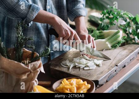 Midsection of young man cutting fennel on board in kitchen Stock Photo
