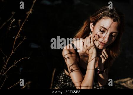 Woman sitting eyes closed in forest under sunlight Stock Photo