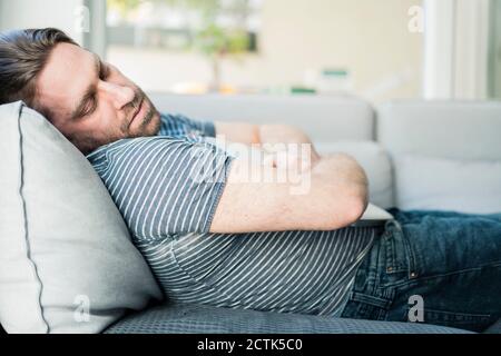 Man with laptop sleeping on sofa in living room Stock Photo