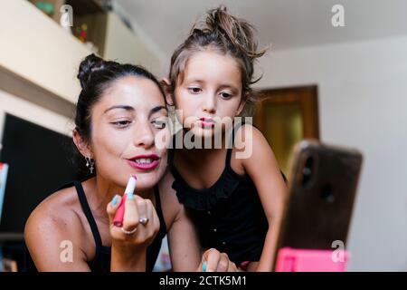 Mother and daughter applying lipstick while video recording in smart phone at home Stock Photo