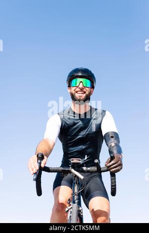 Smiling male amputee cyclist riding bicycle against clear sky Stock Photo