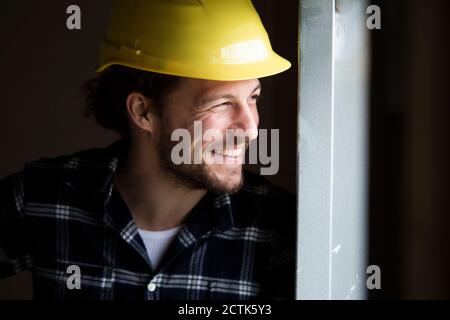 Close-up of smiling construction worker wearing helmet looking away by wall in house Stock Photo