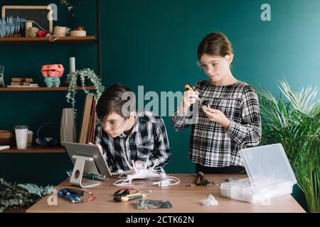 Siblings using digital tablet while preparing drone on table against wall at home Stock Photo