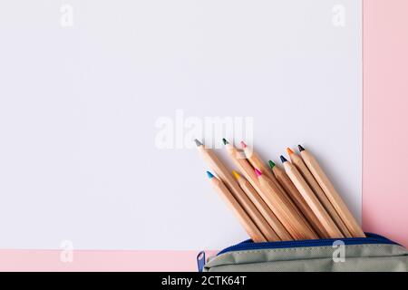 Colored pencils in pouch on blank white paper over pink background Stock Photo