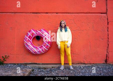 Young woman with dyed hair and floating tyre hanging on red wall Stock Photo