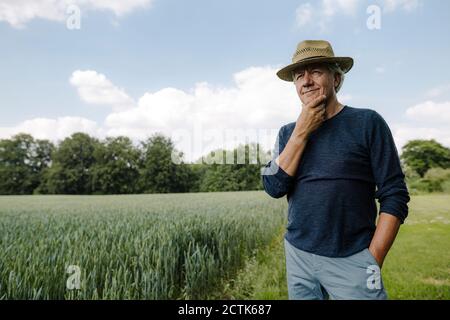 Contemplating man looking away with hand on chin while standing against sky in field Stock Photo
