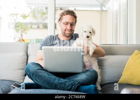 Man using laptop and dog while sitting on sofa Stock Photo