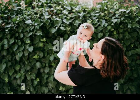 Mother picking up baby girl against ivy Stock Photo