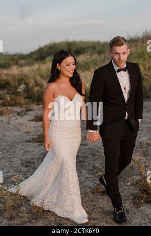 Smiling newlywed holding hands while walking in field Stock Photo